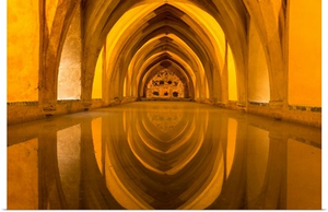 The Arches Of The Interior Of The Baths Reflect In The Calm Water In The Alcazar, Spain